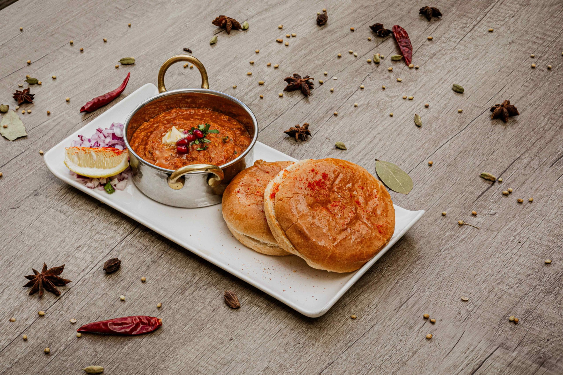 Rich Indian curry in a brass-handled bowl served with soft pav buns at Bukharaa